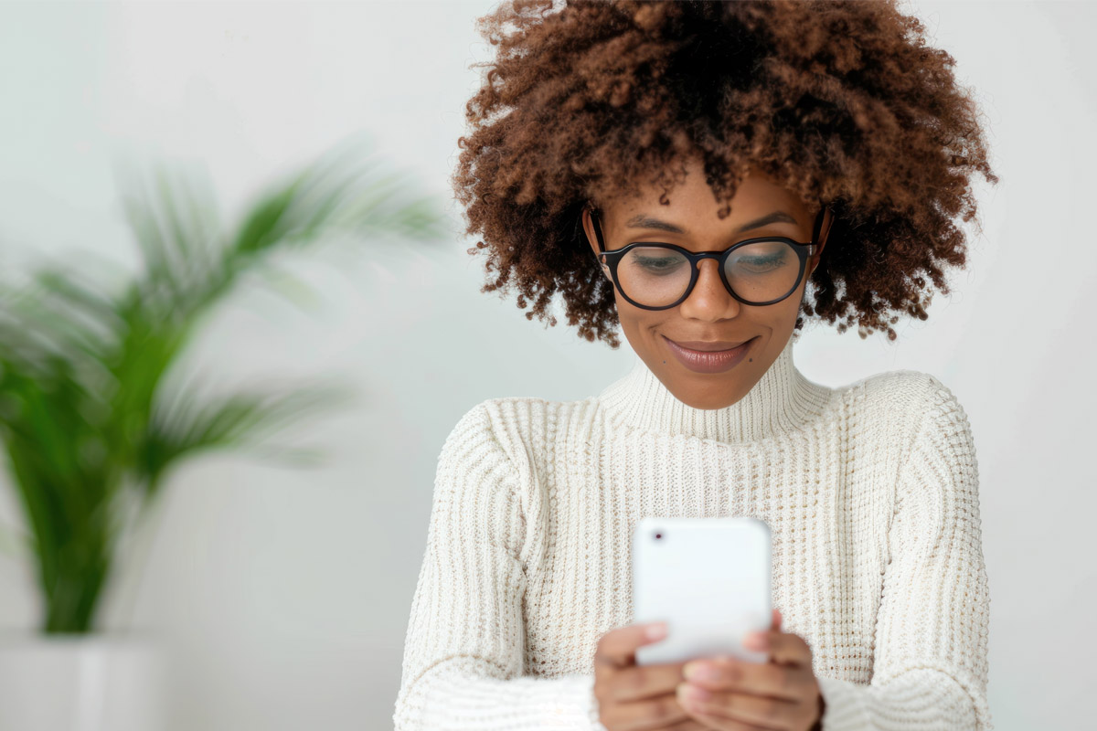 Smiling woman wearing glasses and a white sweater using her smartphone, representing digital communication and email marketing.